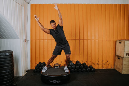 Man in a wide stance on the Power Plate pro5HP with one arm raised overhead