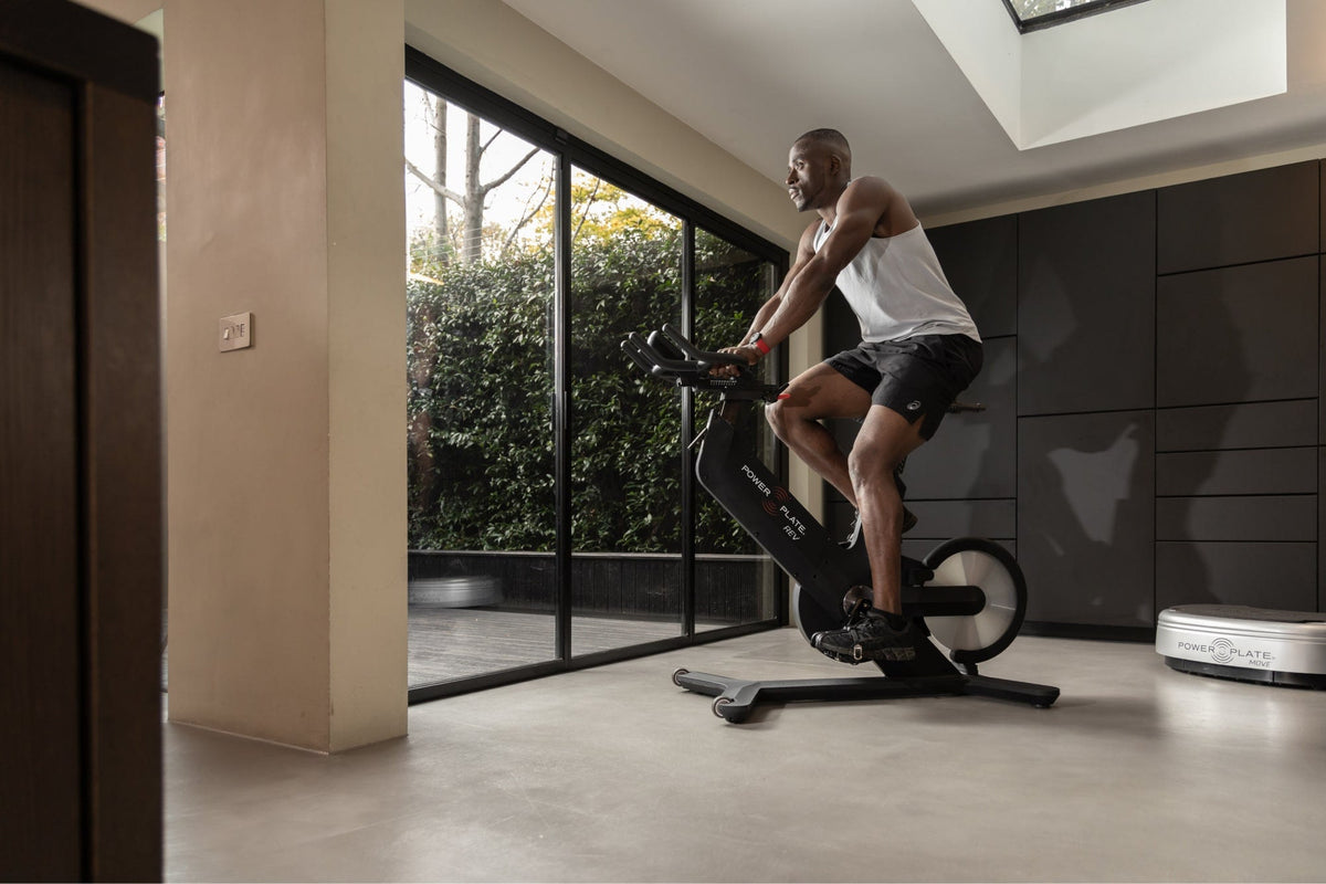 Man riding the Power Plate REV in a home gym with floor to ceiling windows