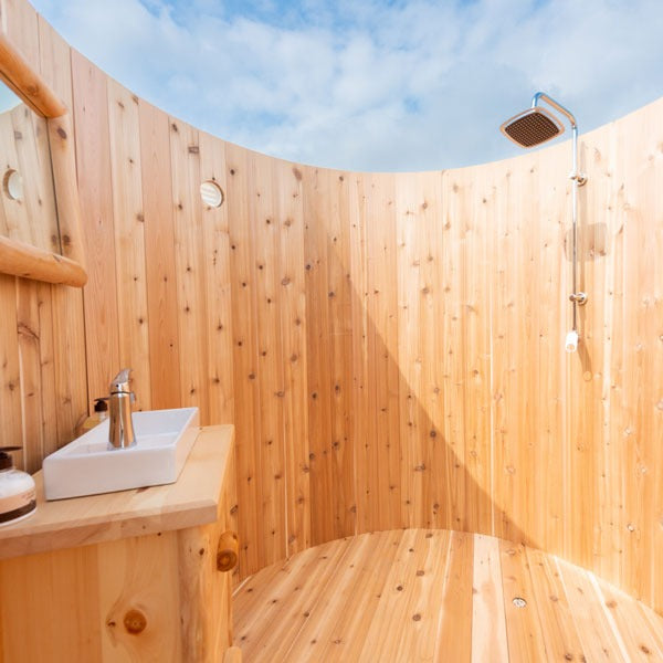 The shower side inside the Skylight: square rain head, riser and hand shower, none included, with the vessel sink at left and sky above.
