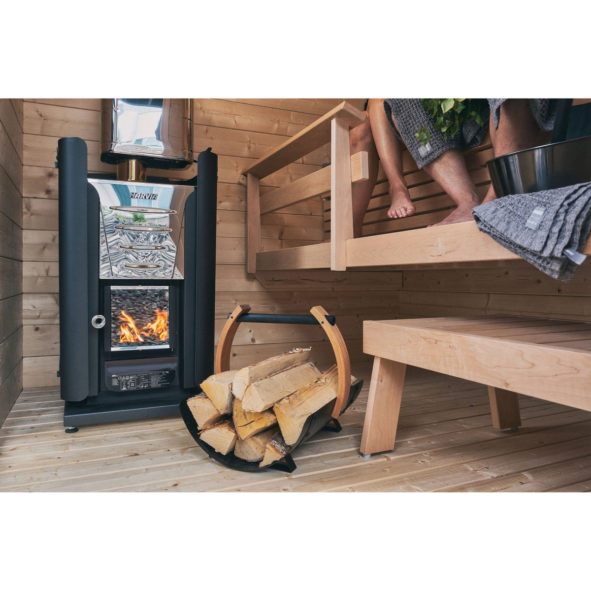 Harvia Pro wood-burning sauna stove beside the bench with firewood stacked