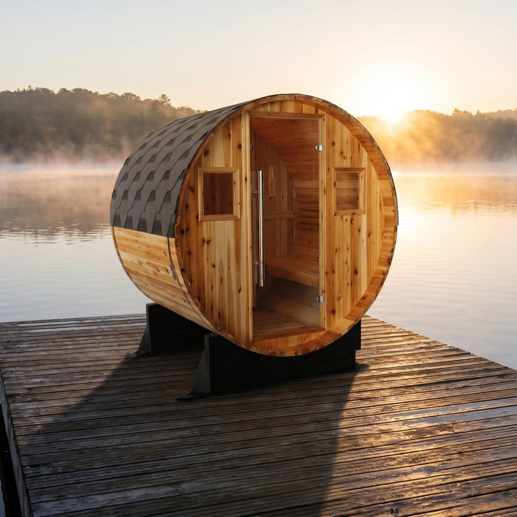 SunRay Aurora barrel sauna for 2 to 4 in western red cedar, glass door and two small windows under the shingled roof, on a wooden dock above a misty lake with the sun rising