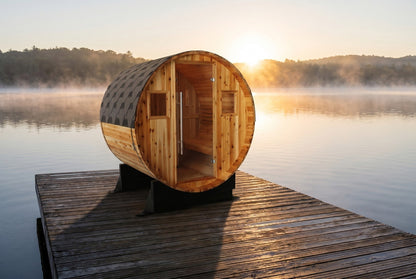 SunRay Aurora barrel sauna in western red cedar on a wooden dock over a misty lake at sunrise: glass door between two small windows under the shingled roof
