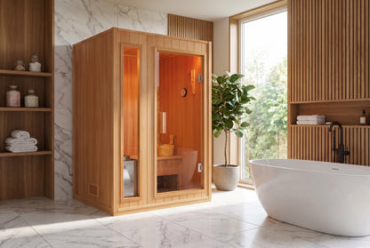 SunRay Baldwin 2-person indoor sauna in hemlock in a bright room with marble walls and a tall window: narrow glass side panel beside the glass door, bench and bucket behind the glass