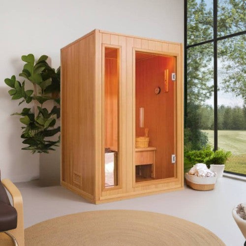 SunRay Baldwin indoor sauna in hemlock beside a tall window with potted plants: glass door and narrow glass side panel, bench and bucket inside