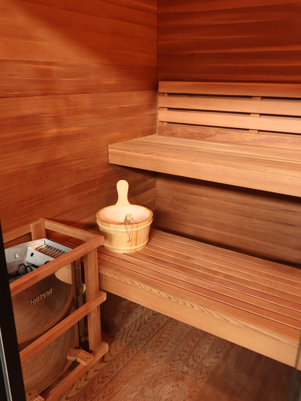 Two-tier benches and Harvia heater in its wooden guard inside the SunRay Cayman, bucket on the lower bench