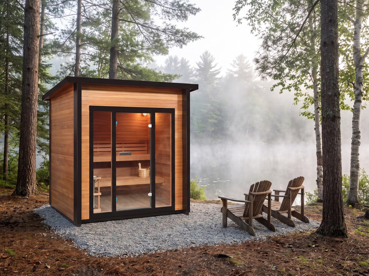 SunRay Cayman 4-person outdoor sauna on a gravel pad among pines by a misty lake, two Adirondack chairs beside the black-framed glass front