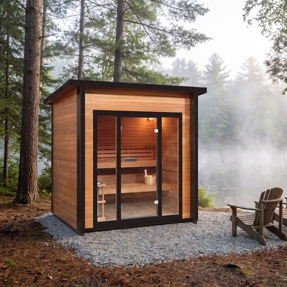 SunRay Cayman outdoor sauna for 4 in hemlock, black framed glass front showing the benches inside, on a gravel pad among tall pines with two Adirondack chairs and a misty lake