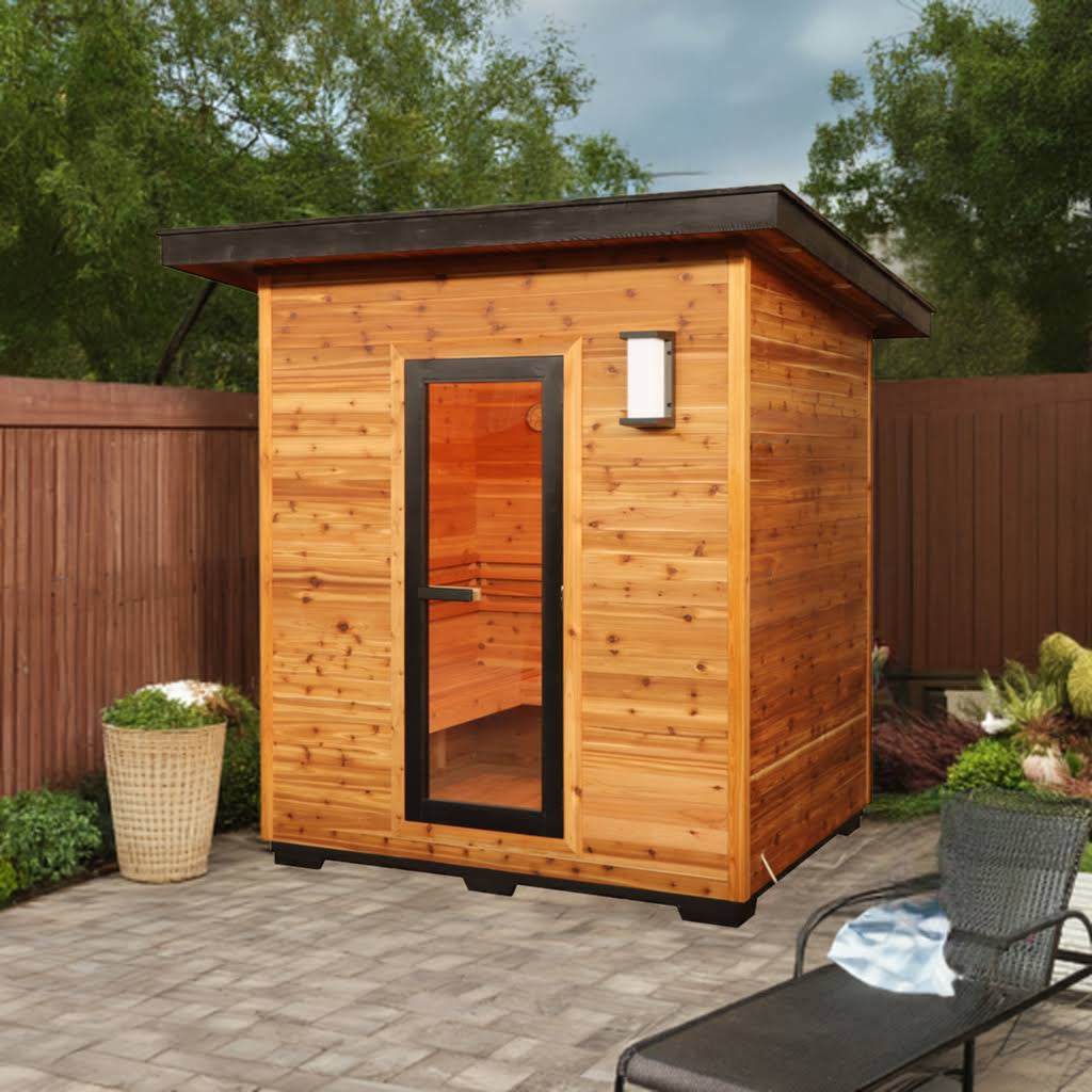 SunRay Denali outdoor sauna for 4 in western red cedar, black framed glass door and wall lantern under the dark roof edge, on a paver patio with a wood fence, planters and a lounge chair