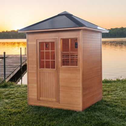 SunRay Freeport outdoor sauna for 3 in hemlock, wooden door with a multi pane window beside the front window under the black pitched roof, on a lakeside lawn next to a dock at sunset