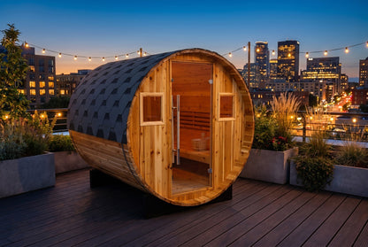 SunRay Galley barrel sauna in western red cedar on a rooftop deck at dusk under string lights, city towers behind