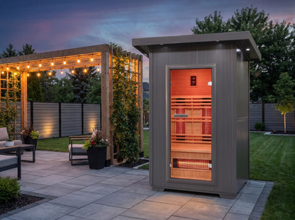 SunRay Logan outdoor infrared sauna on a stone patio at dusk, next to a pergola with string lights