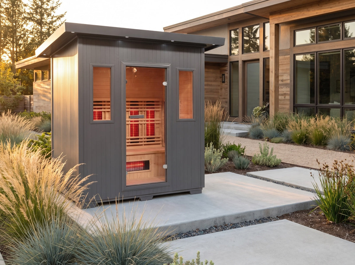 SunRay Pacific outdoor infrared sauna on a concrete path beside a modern house, among ornamental grasses