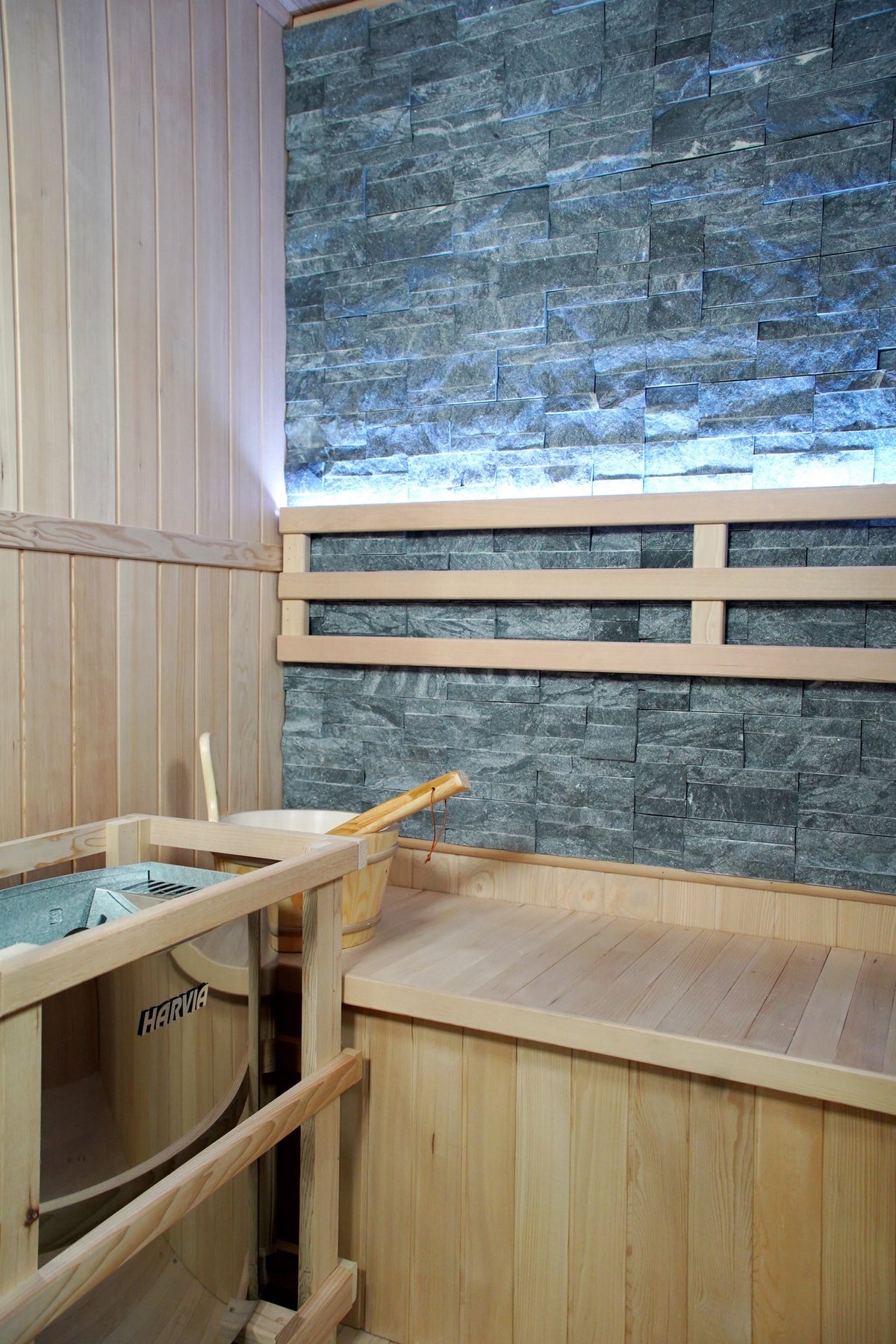 Stone back wall with lit ledge, backrest and bench inside the SunRay Rockledge, Harvia heater in its wooden guard