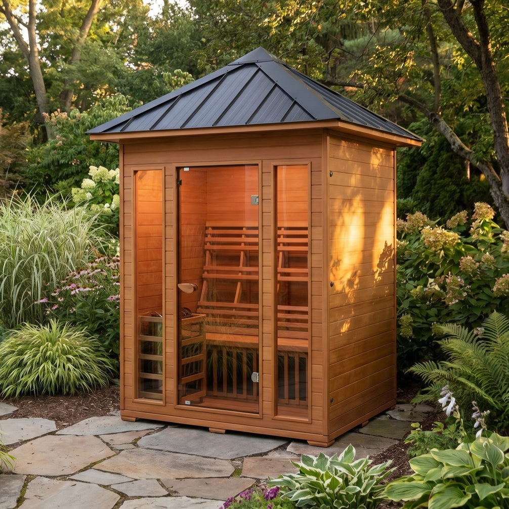 SunRay Waverly 3-person outdoor sauna on a flagstone path in a planted garden: black pitched roof, glass door between two glass front windows, backrest and heater guard visible inside