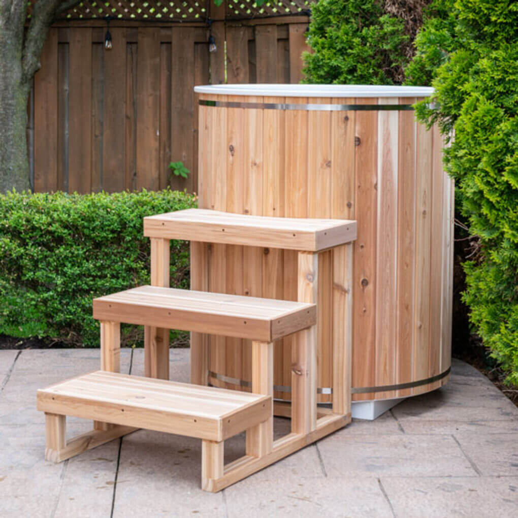 The Baltic Plunge Tub on a backyard patio with cedar steps and cedar lid in place, hedge behind