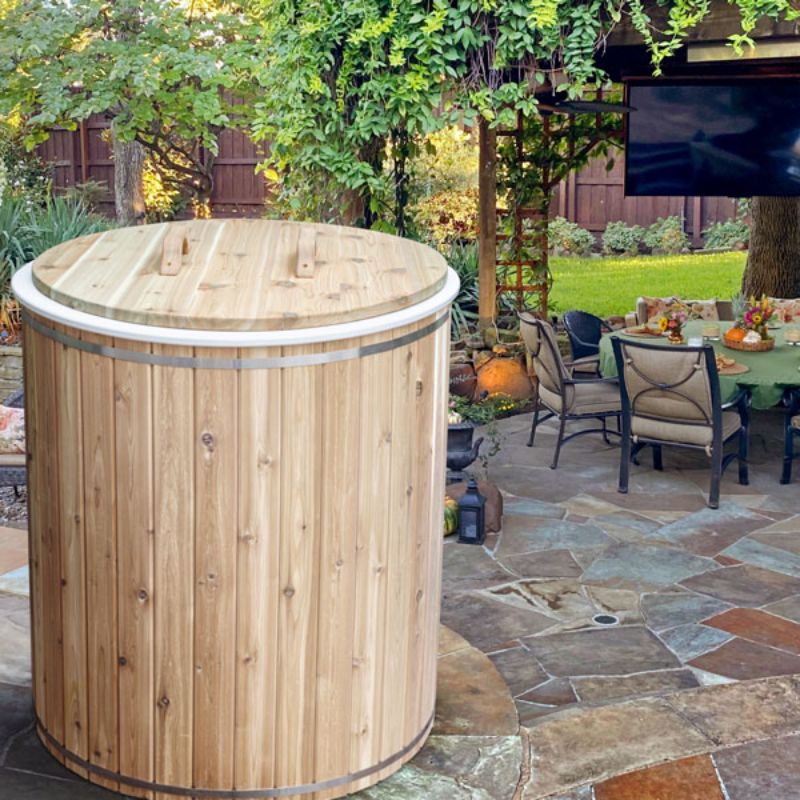 The Baltic Plunge Tub with cedar lid on a flagstone patio beside outdoor dining