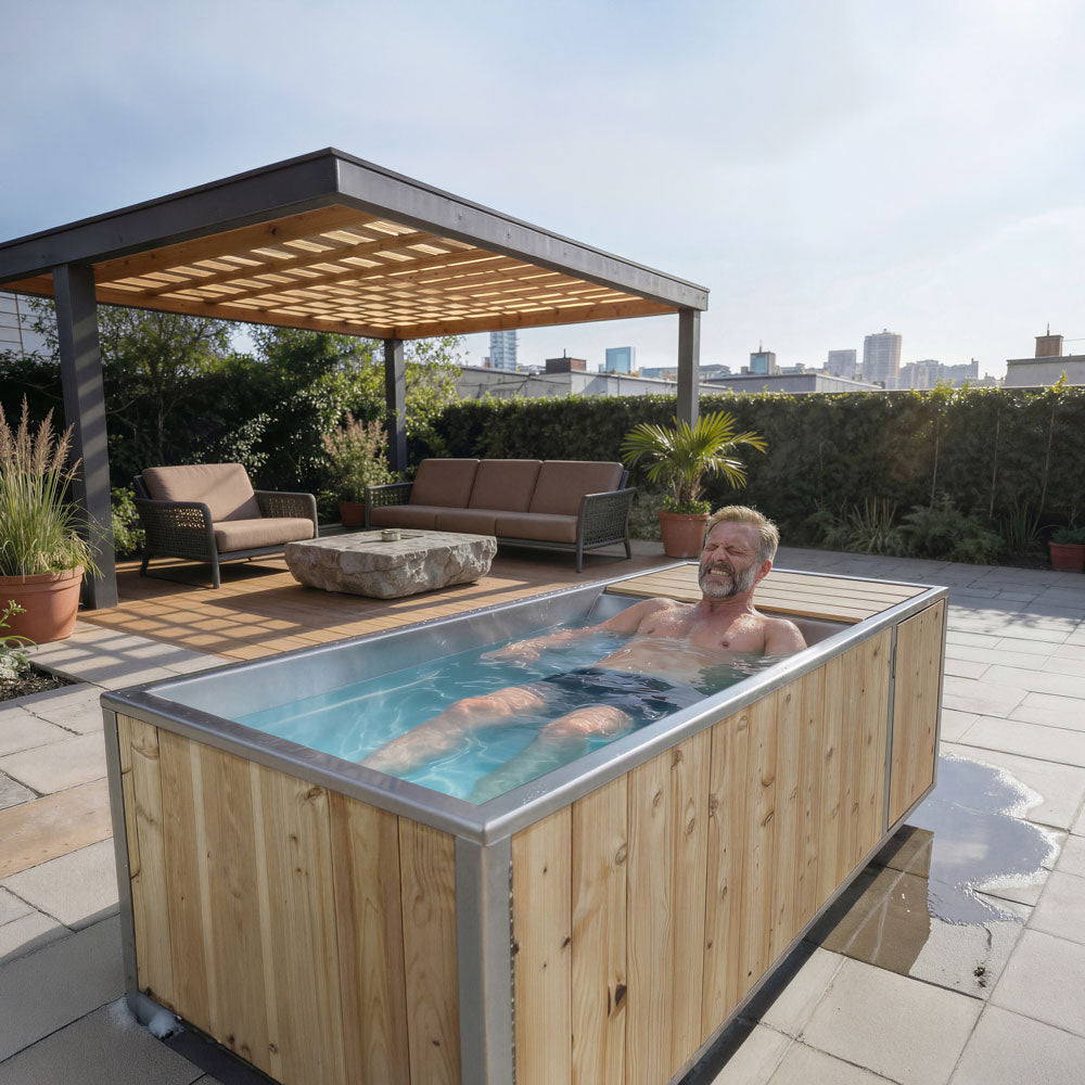 Man relaxing in The Flow Cold Plunge on a rooftop patio under a pergola, stainless interior filled with water