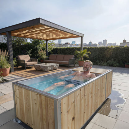 Man relaxing in The Flow Cold Plunge on a rooftop patio under a pergola, stainless interior filled with water