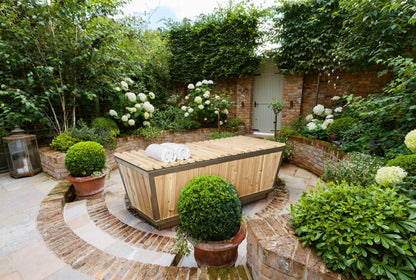 The Polar Plunge Tub in a walled courtyard garden with the cedar roll-up cover closed and rolled towels on top
