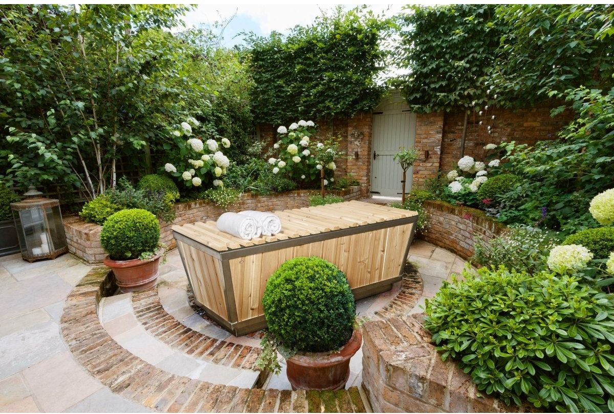The Polar Plunge Tub in a walled courtyard garden with the cedar roll-up cover closed and rolled towels on top