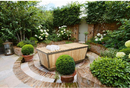 The Polar Plunge Tub in a walled courtyard garden with the cedar roll-up cover closed and rolled towels on top