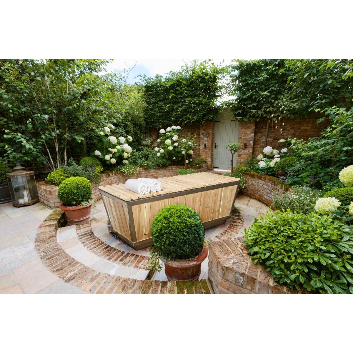 The Polar Plunge Tub in a walled courtyard garden with the cedar roll-up cover closed and rolled towels on top