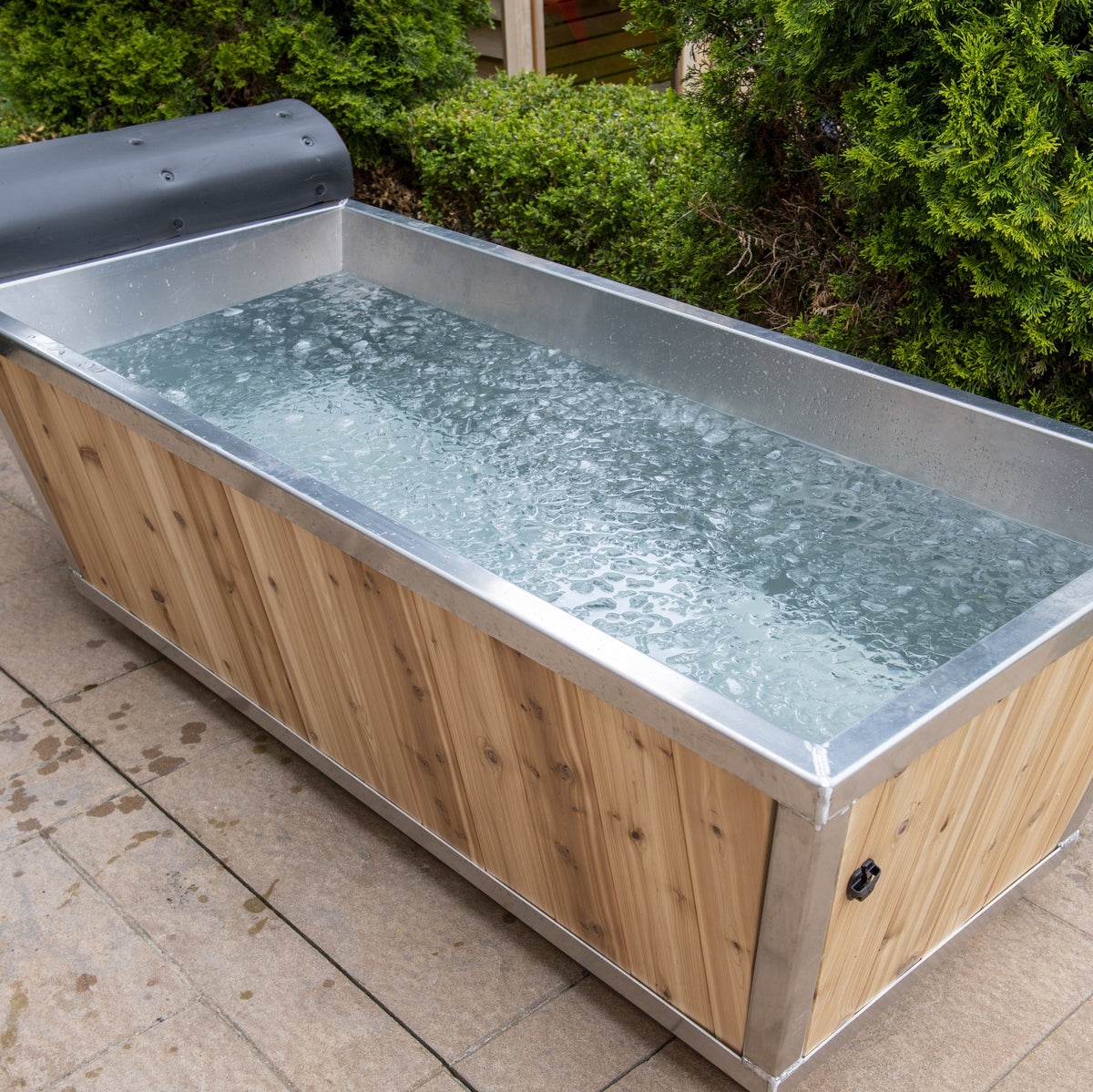 The Polar Plunge Tub filled with water on a patio, stainless interior and rolled-back cedar cover