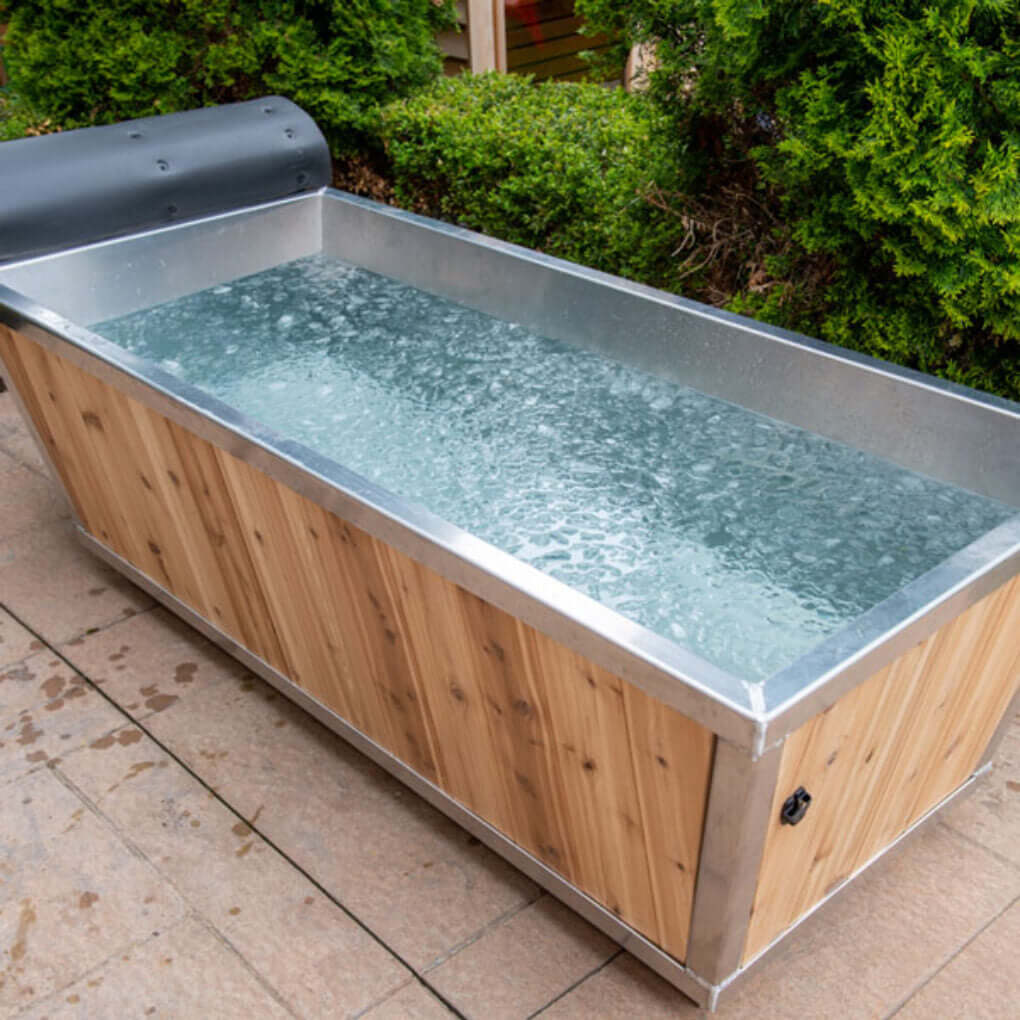The Polar Plunge Tub filled with water on a patio, stainless interior and rolled-back cedar cover