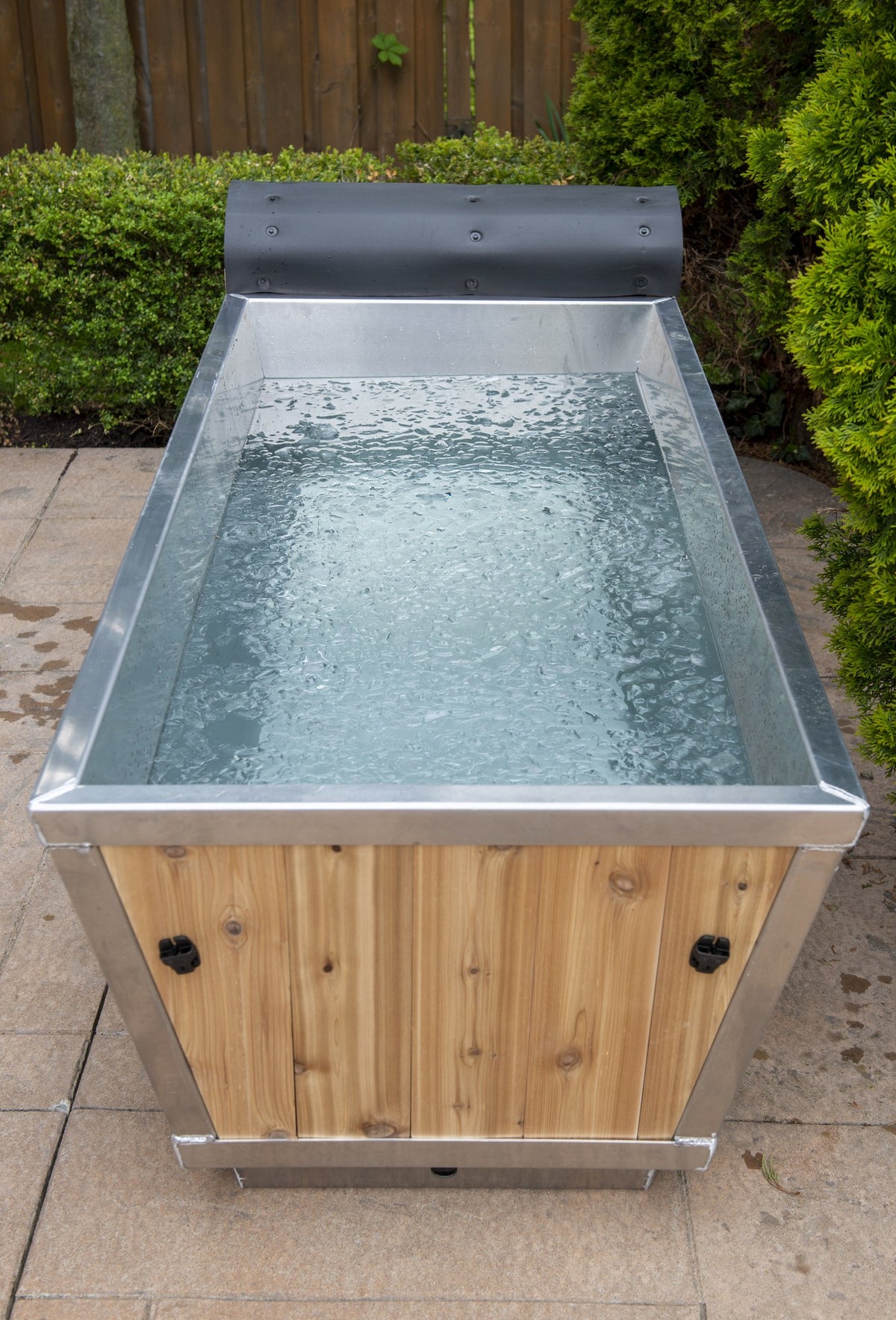 Front view of The Polar Plunge Tub filled with water, cedar roll-up cover pushed back
