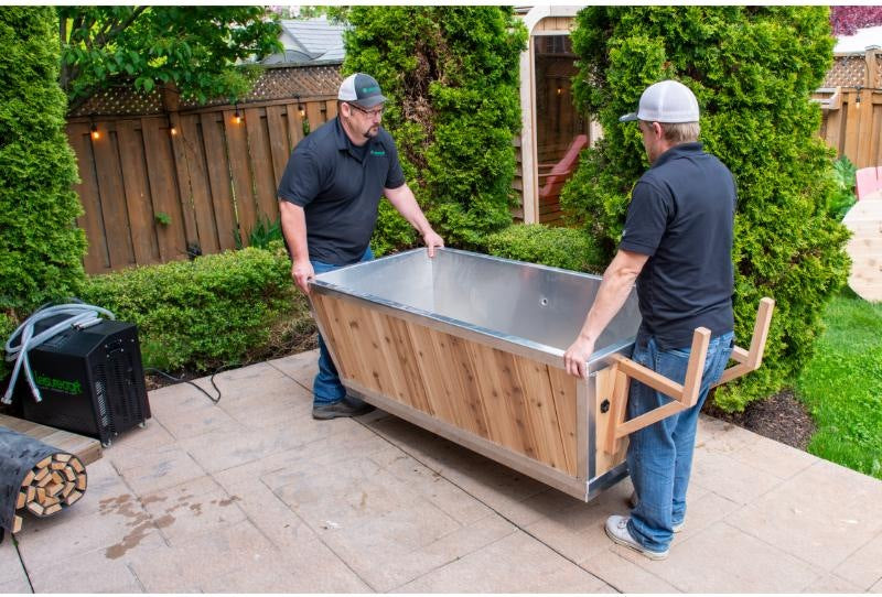 Two people carrying the empty Polar Plunge Tub across a patio, stainless interior visible