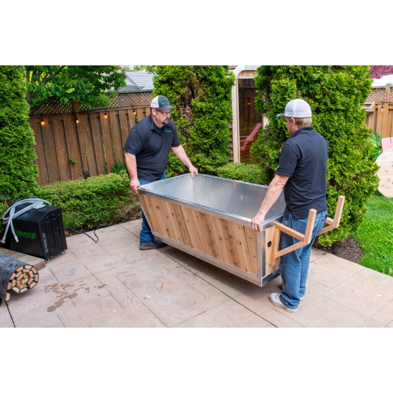Two installers carrying the empty Polar Plunge Tub across a patio, stainless interior visible