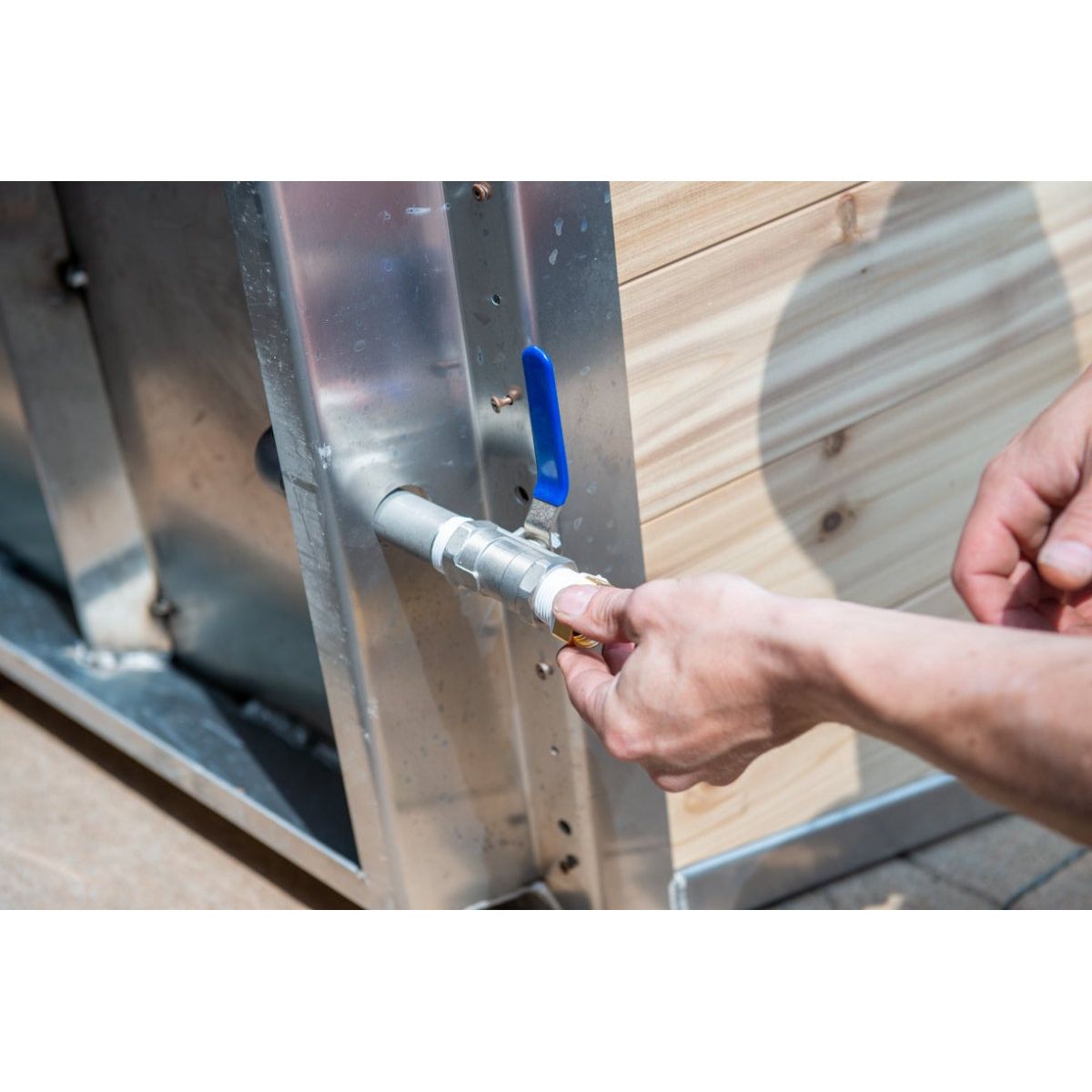 Hand-tightening the chiller inlet fitting on the stainless wall of The Polar Plunge Tub