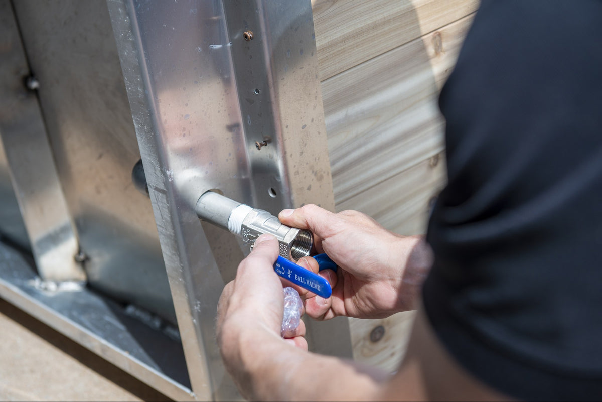 Threading a fitting onto the blue-handled ball valve at the end wall of The Polar Plunge Tub