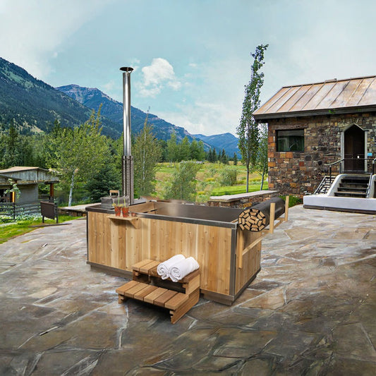 The Starlight Wood Burning Hot Tub on a flagstone patio below mountains, chimney at the stove end, shown with the optional aluminum interior and roll-up cover.